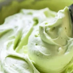 Pistachio buttercream frosting in a bowl with a spatula swirl